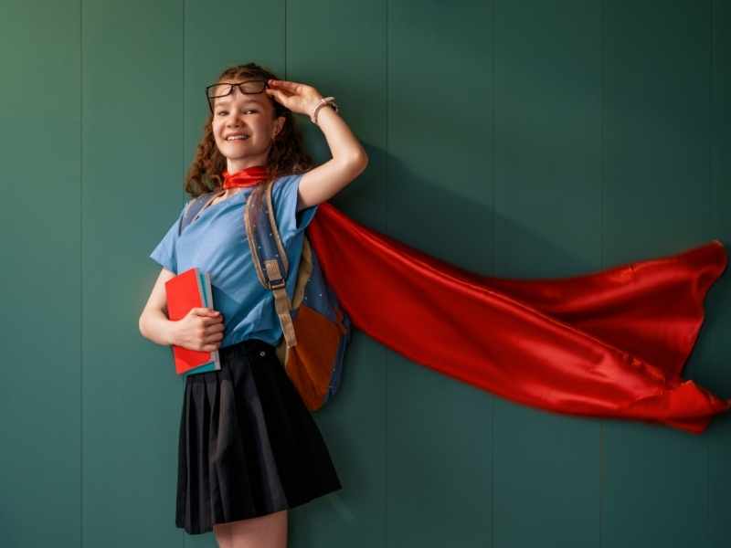 Estudiante con capa roja frente a un pizarrón, representando que dormir bien mejora el rendimiento escolar.