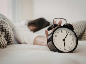 Reloj despertador junto a una persona durmiendo, símbolo de horarios de sueño y descanso para estudiantes.